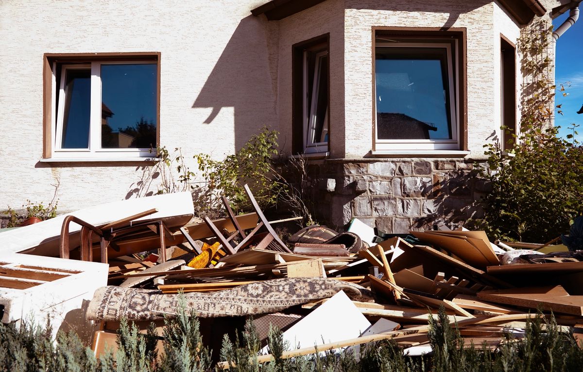 Un tas de meubles et de débris abandonnés devant une maison aux murs beiges