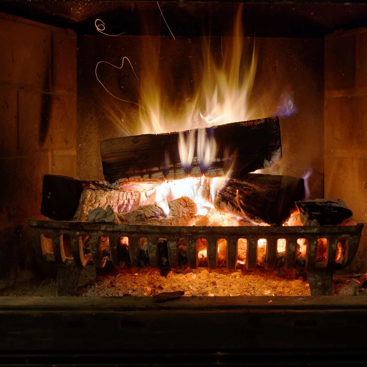 Roaring wood fire burning in a masonry fireplace with glowing embers and cast iron grate, Flue Pros 