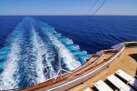 View from a cruise ship deck showing ocean wake and seating area.
