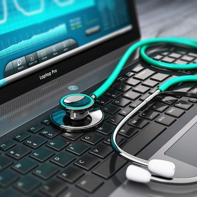 A stethoscope resting on a laptop keyboard with medical data on screen.