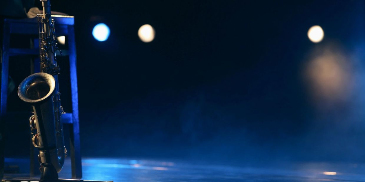A saxophone rests on a stage with blue spotlights in the background.