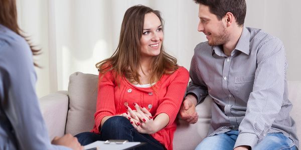 a couple sat looking at each other and smiling. a women sat opposite them with a clipboard