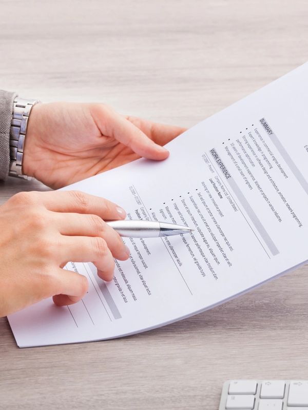 Person reviewing a resume with a pen in hand over a desk.