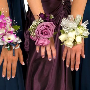 Three hands with elegant corsages and manicured nails at a formal event.