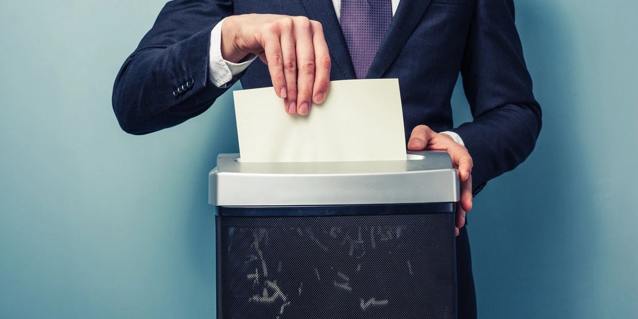 Businessman shredding a paper document in an office shredder.