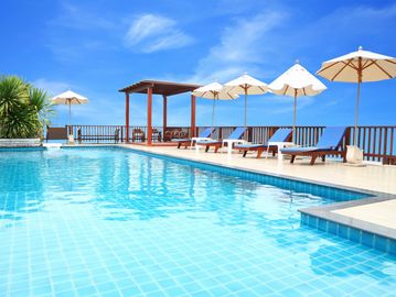 Bright outdoor pool with lounge chairs and umbrellas under a clear blue sky.