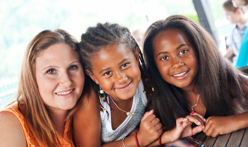 Woman and two young girls smiling together with their arms in front of them on the table