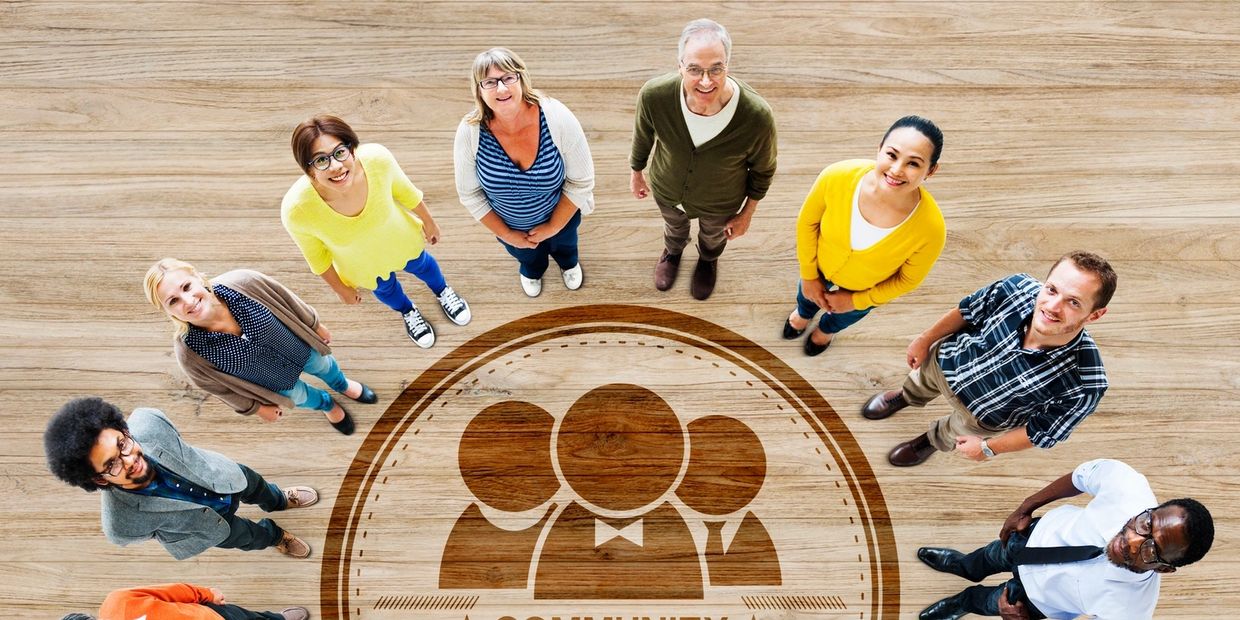 Diverse group standing around community emblem on wooden floor.