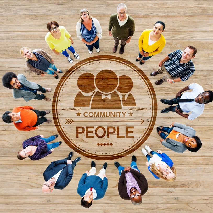 Diverse group standing in a circle around a community emblem on wooden floor.