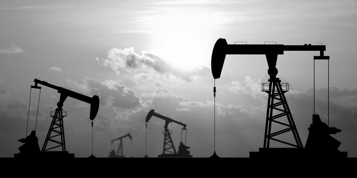 Silhouettes of oil pump jacks against a cloudy sky.