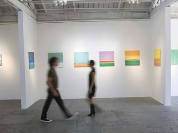 Two people walk past colorful abstract paintings in a modern gallery space.