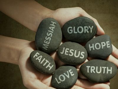 Hands holding stones with words like Jesus, Faith, and Hope symbolizing spirituality.
