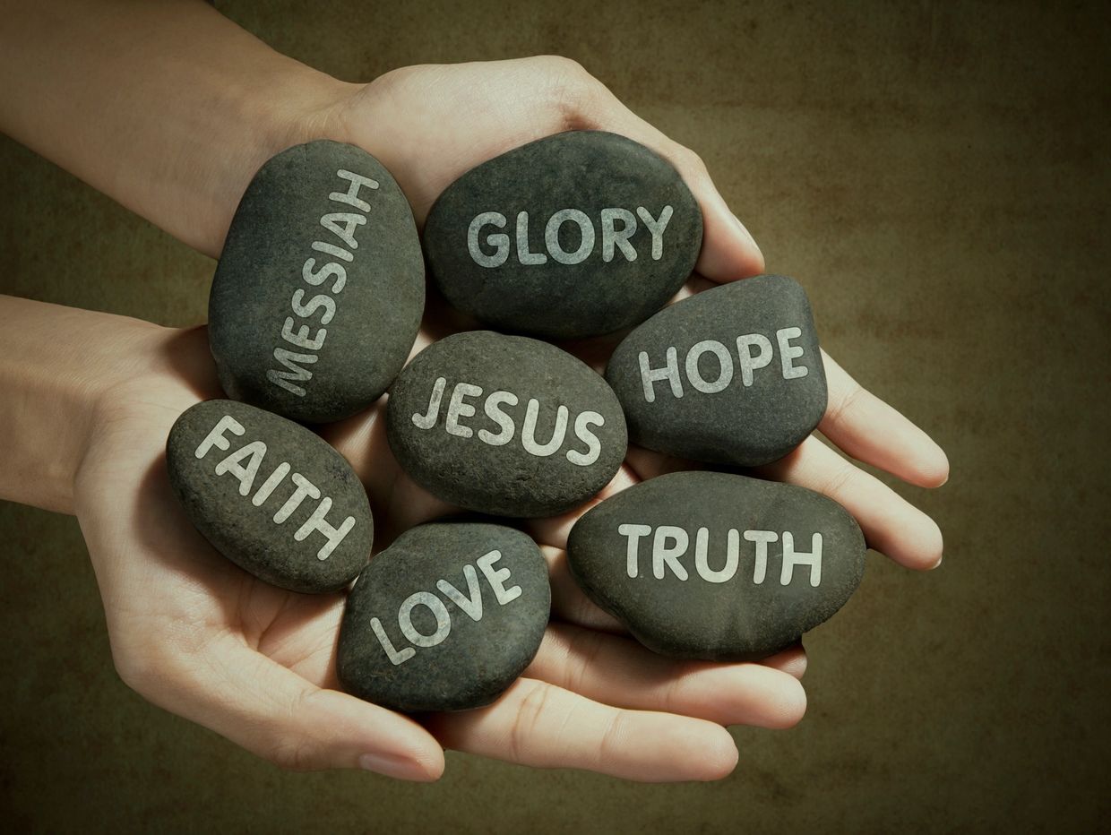 Hands holding stones engraved with faith and hope words.