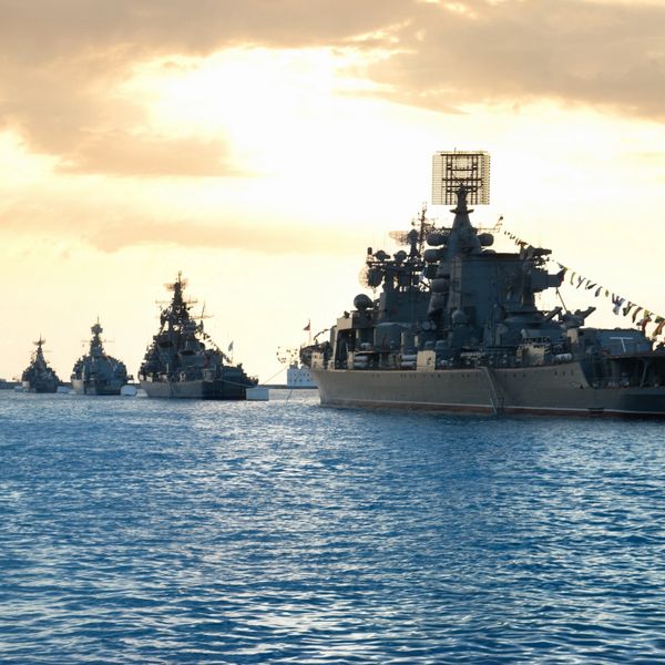A fleet of warships sailing on the sea during sunset.