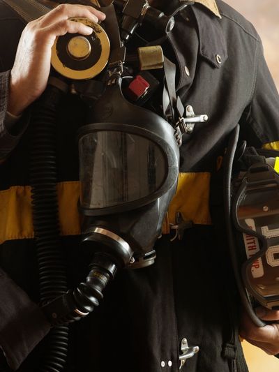 Firefighter in turnout gear holding a helmet and breathing mask
