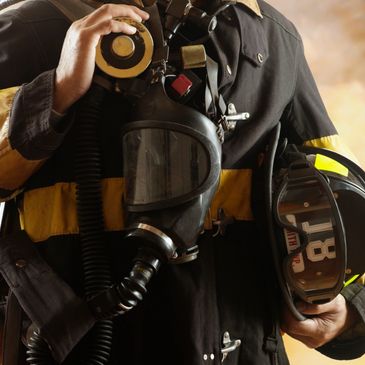 Firefighter holding a gas mask and helmet in uniform.