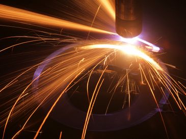 Bright sparks fly from metal cutting with a plasma torch in a dark setting.