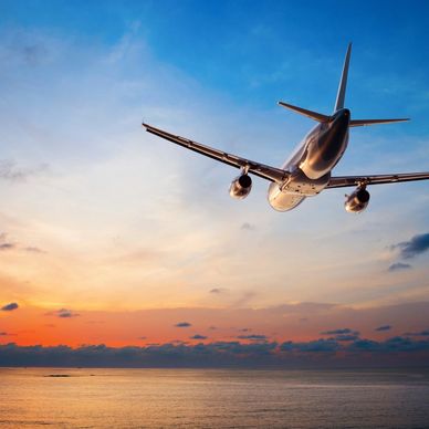 Airplane flying over the ocean at sunset.