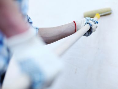 Person painting a wall with a roller while wearing gloves.