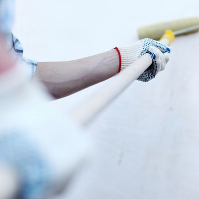 Person holding a paint roller with a gloved hand, painting a wall.