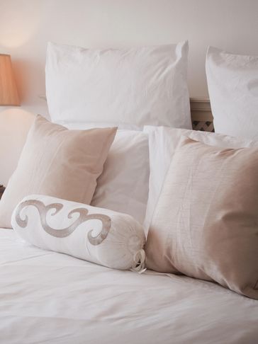 Cozy bed with white and beige pillows and a soft-lit lamp.