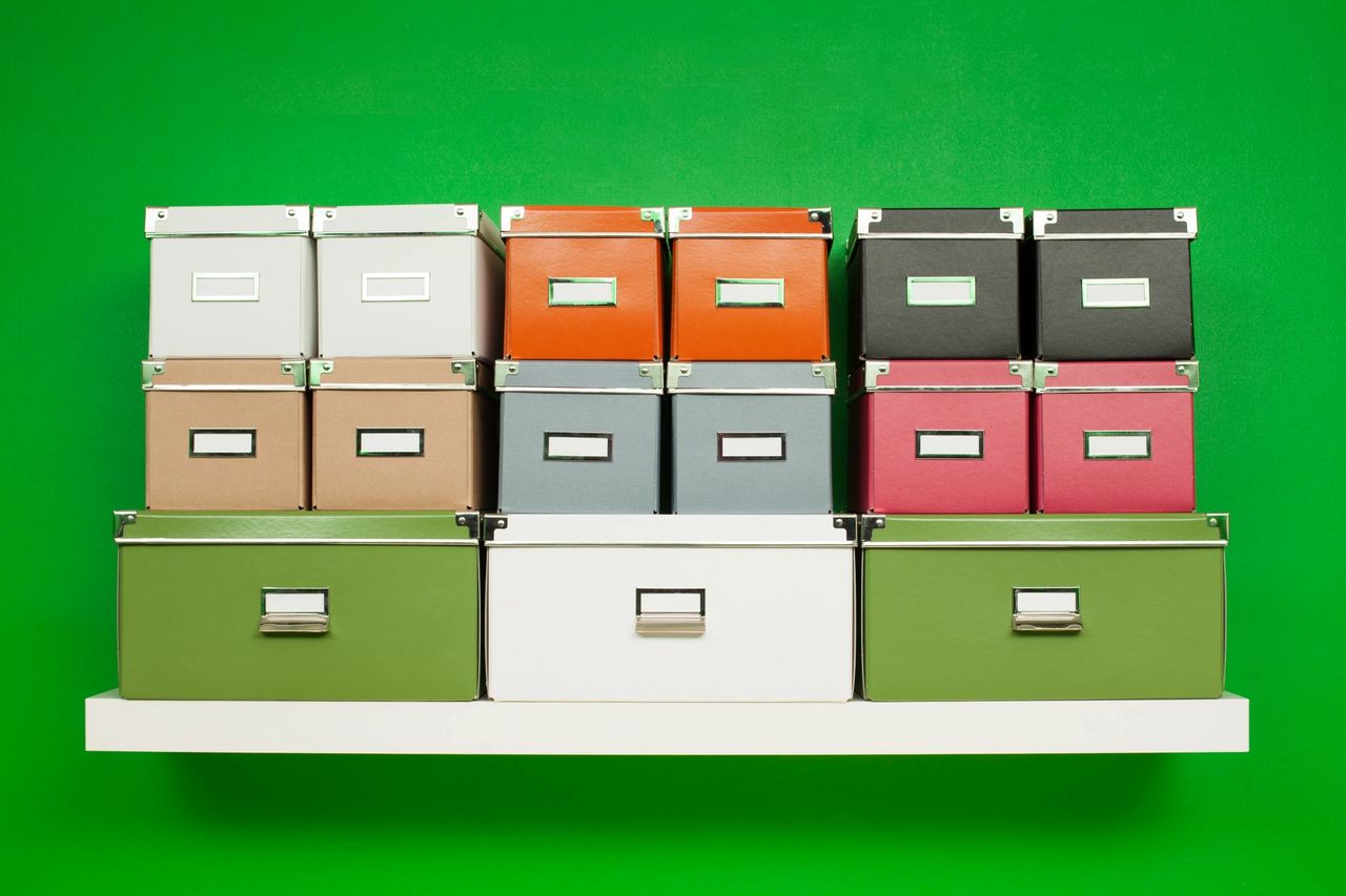 Many colorful boxes of files sit on a bookshelf in-front of a bright green wall.