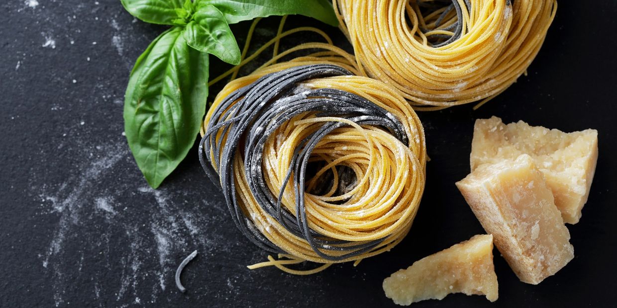 Nests of fresh pasta with basil leaves and Parmesan cheese on a dark surface.