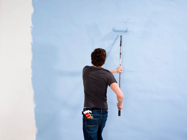 Man painting a wall light blue with a roller.