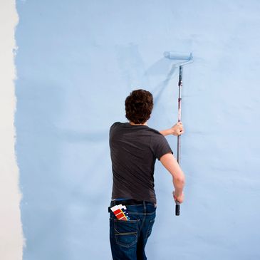 Man painting a wall with light blue paint.