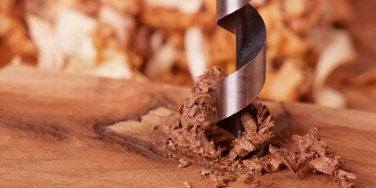 Close-up of a drill bit boring into wood, creating wood shavings.