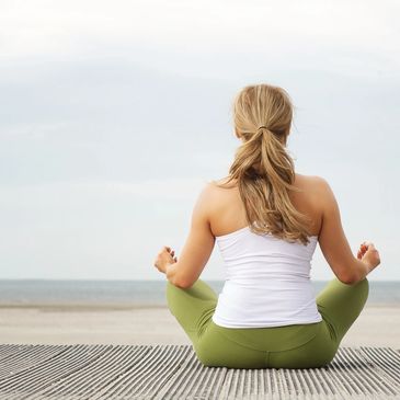 A Yoga student sat facing the ocean in her meditation pose with hands on her knees feeling relaxed.