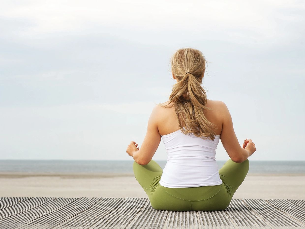 Woman practicing yoga meditation facing the beach and ocean.