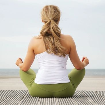 Woman meditating in lotus pose by the beach, facing the sea.