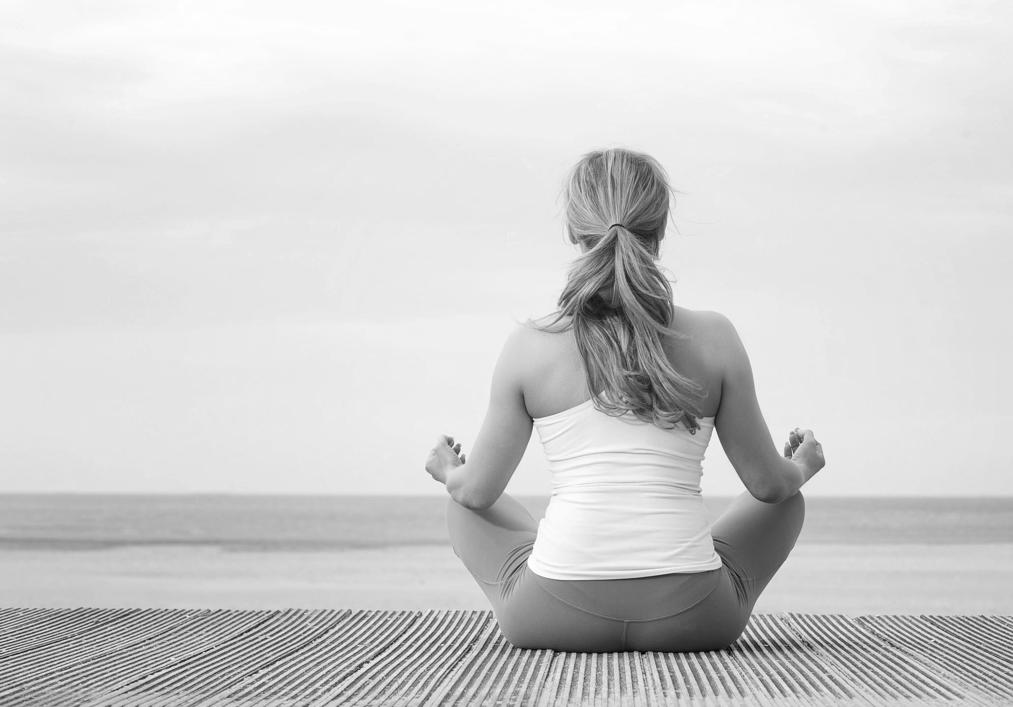 Woman sitting on beach facing water in meditation