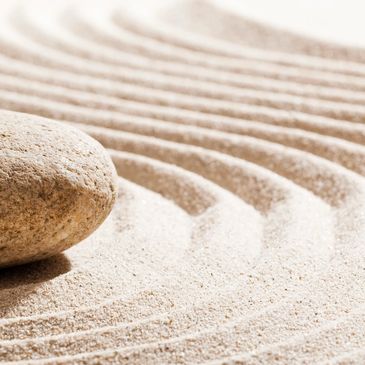 Close-up of a smooth stone on raked sand with curved patterns.