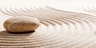 A stone on raked sand with curved lines.