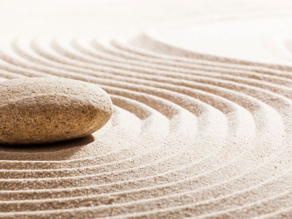 Smooth stone on raked sand with curved lines.