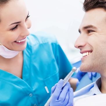 A photo of a female dentist holding a dental handpiece and smiling at a male patient.