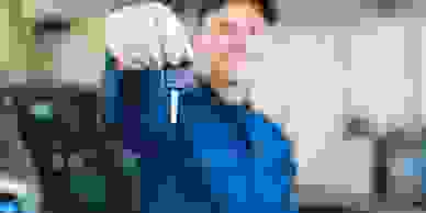 A mechanic holding up a car key in a white glove.