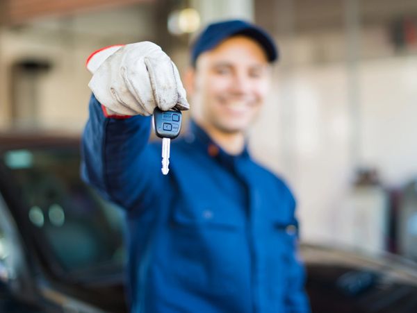Man in blue uniform holding a car key towards the camera.