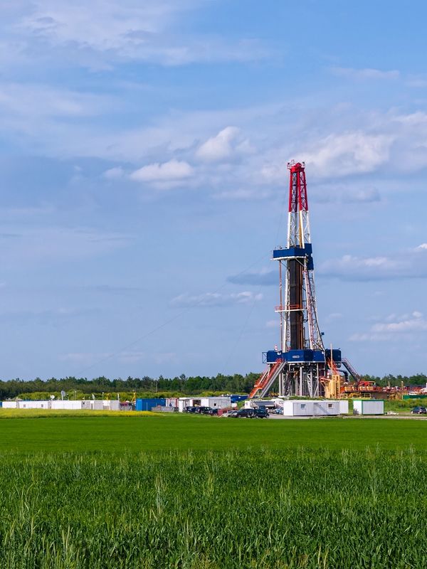 An oil drilling rig stands in a green field under a partly cloudy sky.