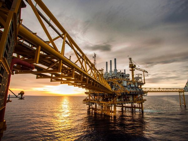 An offshore oil rig at sunset over the ocean.