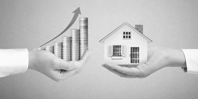 Hands holding stacked coins with upward arrow and a house model representing investment growth.