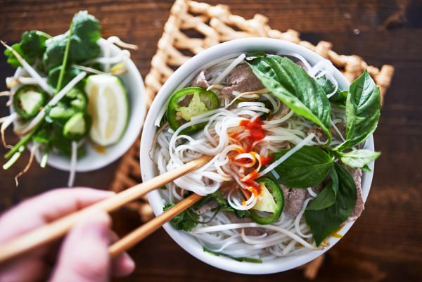 Bowl of pho with fresh herbs, jalapeño, and chopsticks.