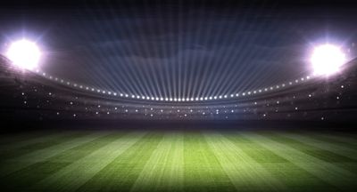 Empty illuminated stadium field at night under bright floodlights.