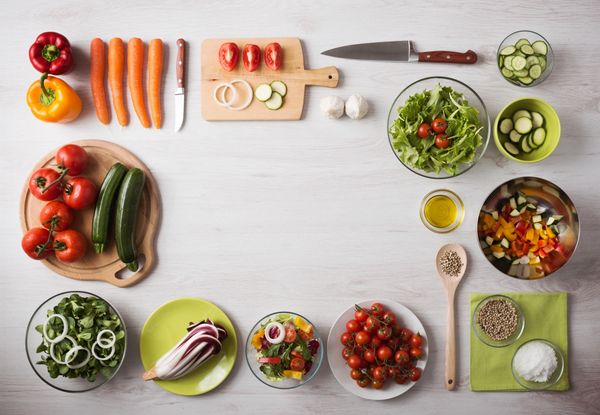 Fresh vegetables and salad ingredients arranged neatly on a white table.
