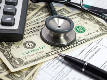 Stethoscope on a couple of dollar bills, next to a keyboard.