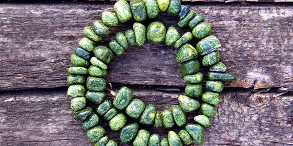 Green stone beads strung together, placed on rustic wooden surface.