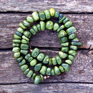 a coiled necklace of green stones laying against a piece of weathered wood