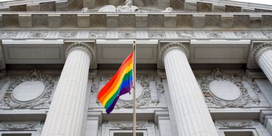 rainbow flag in front of and under facade of large courthouse building with columns